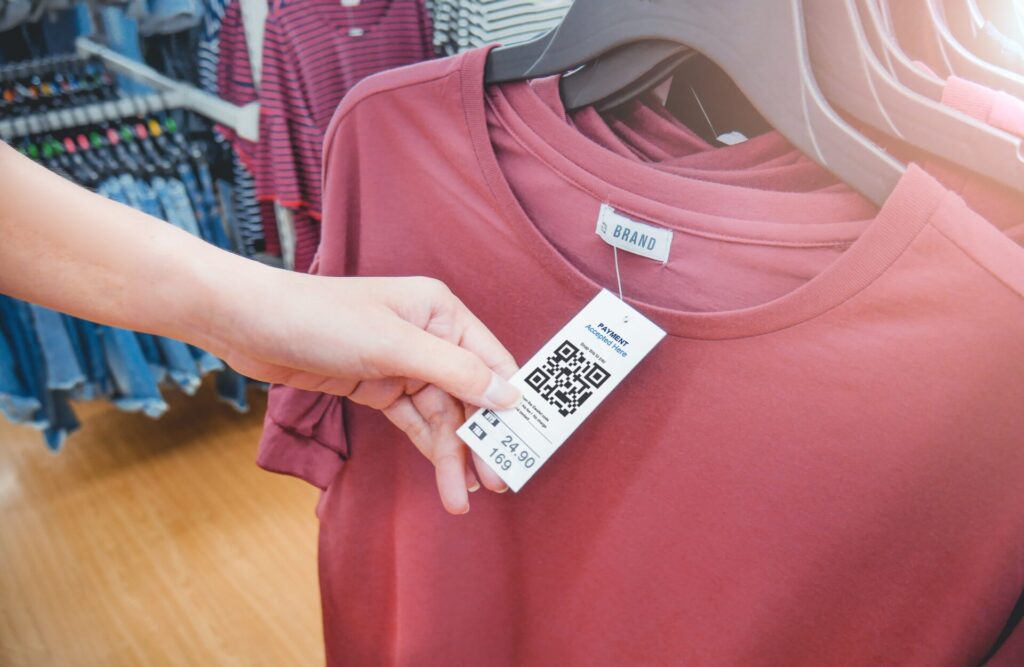 Woman's hand with a cloth hang tag label with QR code in a clothing shop.